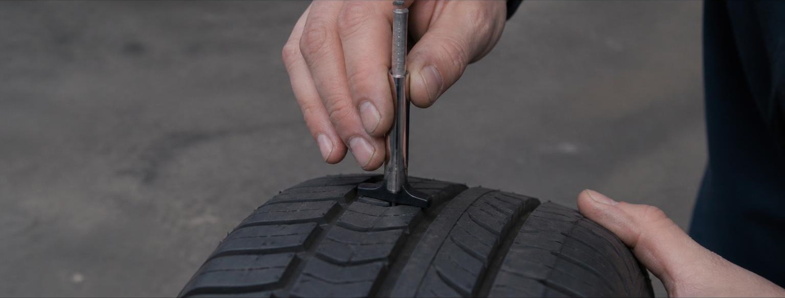 A technician measuring tyre tread depth with a gauge.